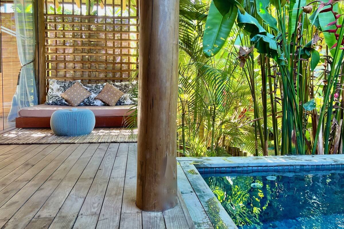 A wooden deck with a seating area, a pool, and lush tropical plants.