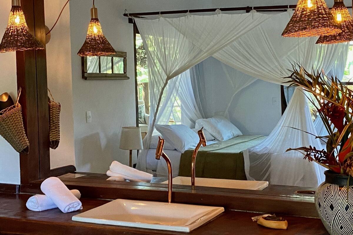 A bedroom with a canopy bed, a large mirror, a sink, and two hanging lamps.