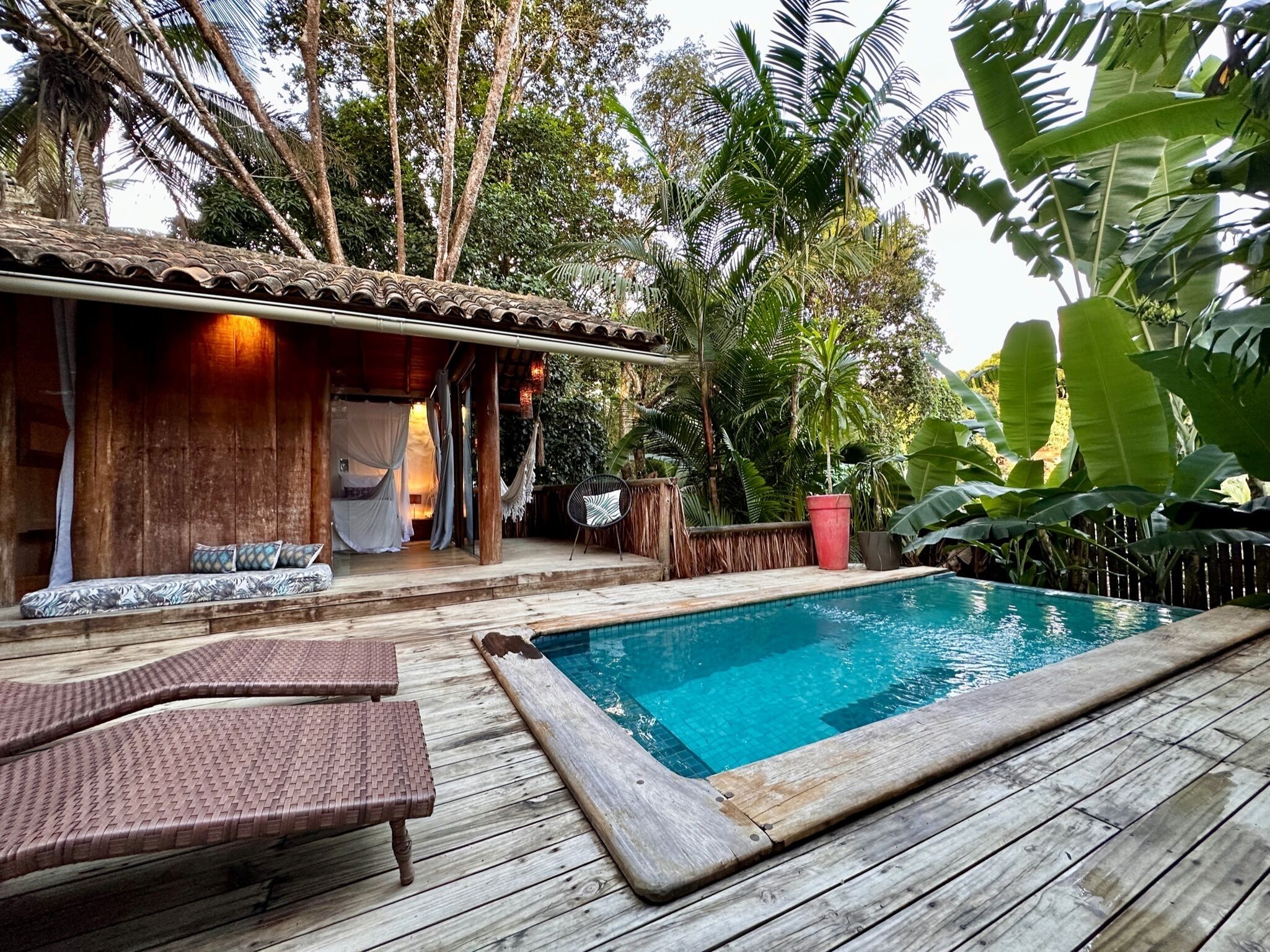 A wooden deck with a pool, a covered seating area, and lush tropical vegetation.