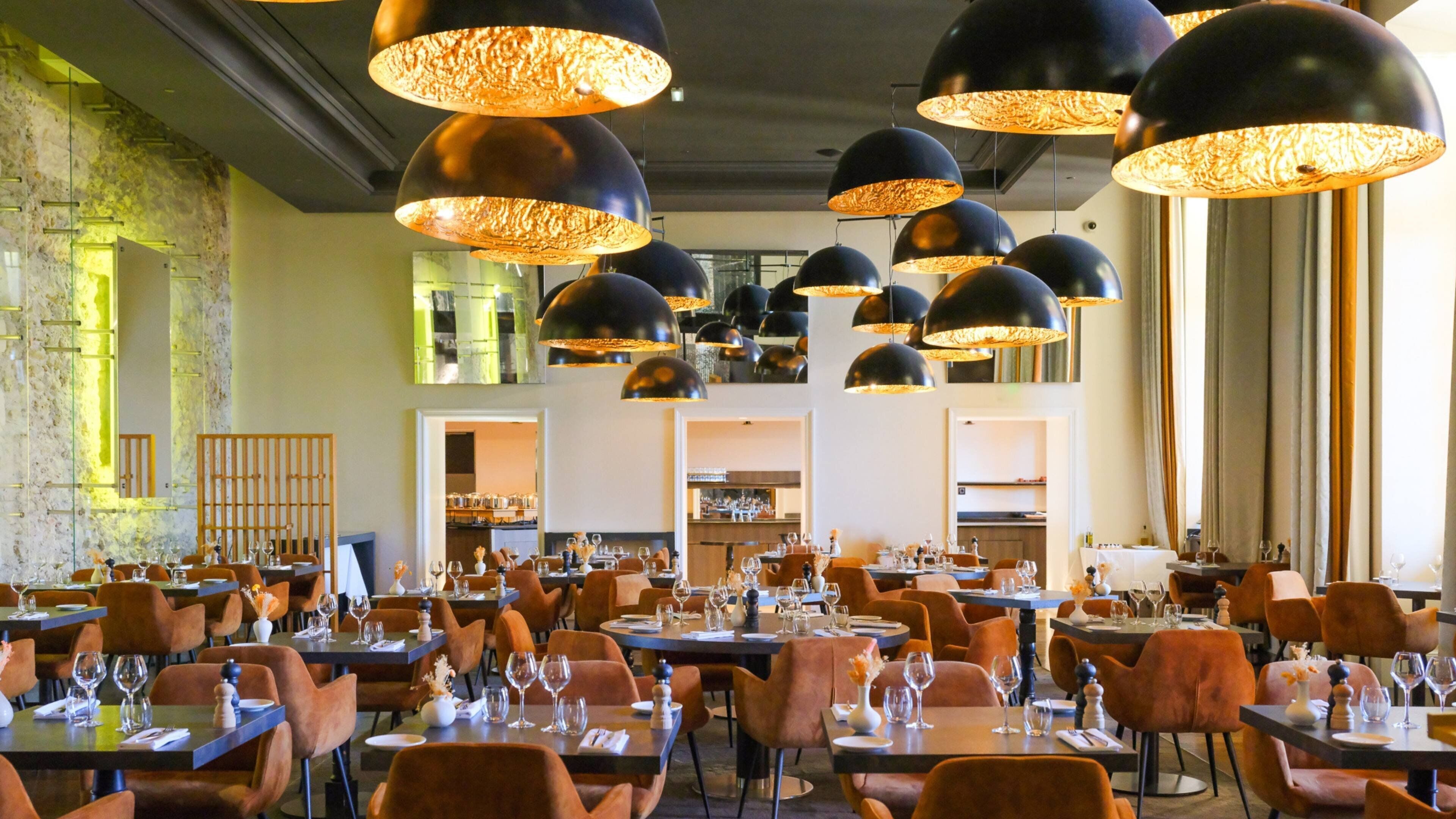 A restaurant with multiple dining tables, black pendant lights, and orange chairs.