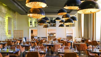 A restaurant with multiple dining tables, black pendant lights, and orange chairs.