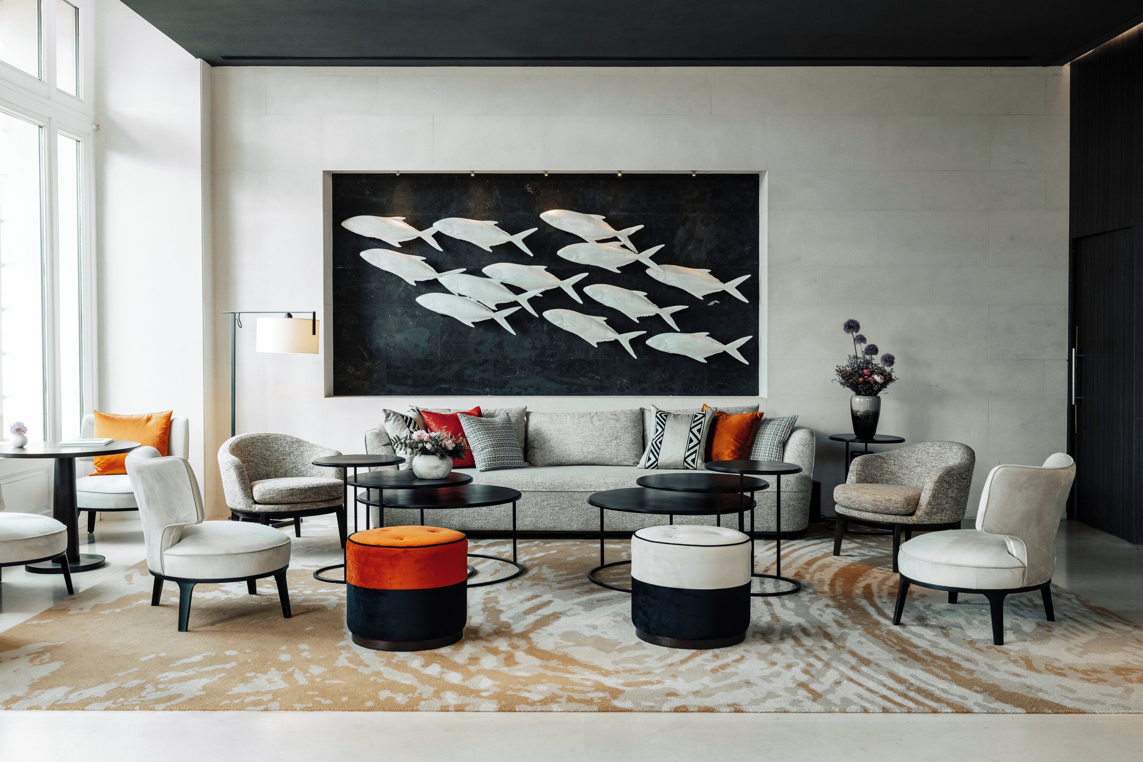 A modern living room with a large abstract fish painting, a grey sofa with patterned cushions, and a mix of round and square coffee tables.