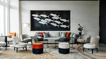 A modern living room with a large abstract fish painting, a grey sofa with patterned cushions, and a mix of round and square coffee tables.