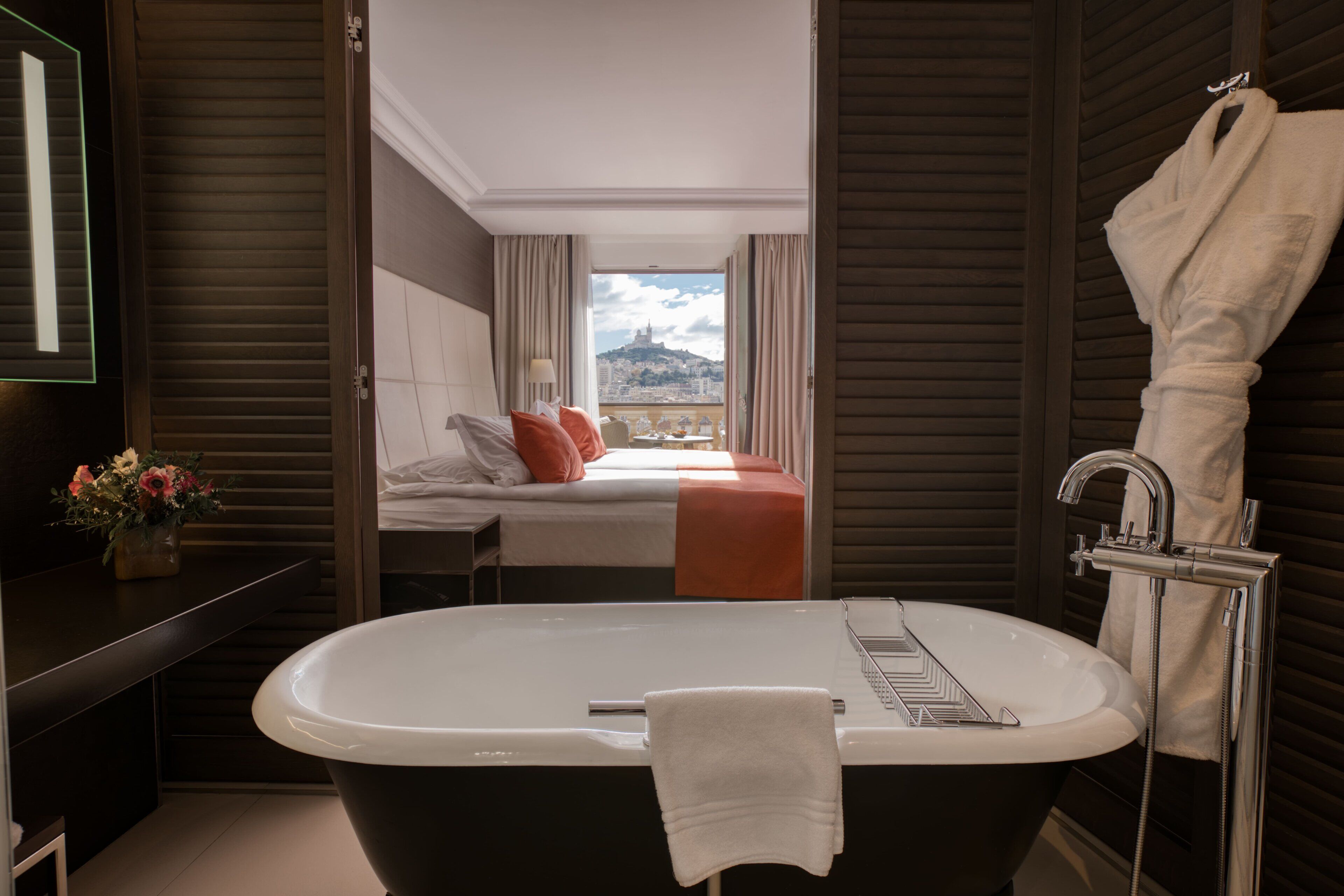 Un baño moderno con bañera, lavabo y ducha. Se ve una cama con vistas a la ciudad.