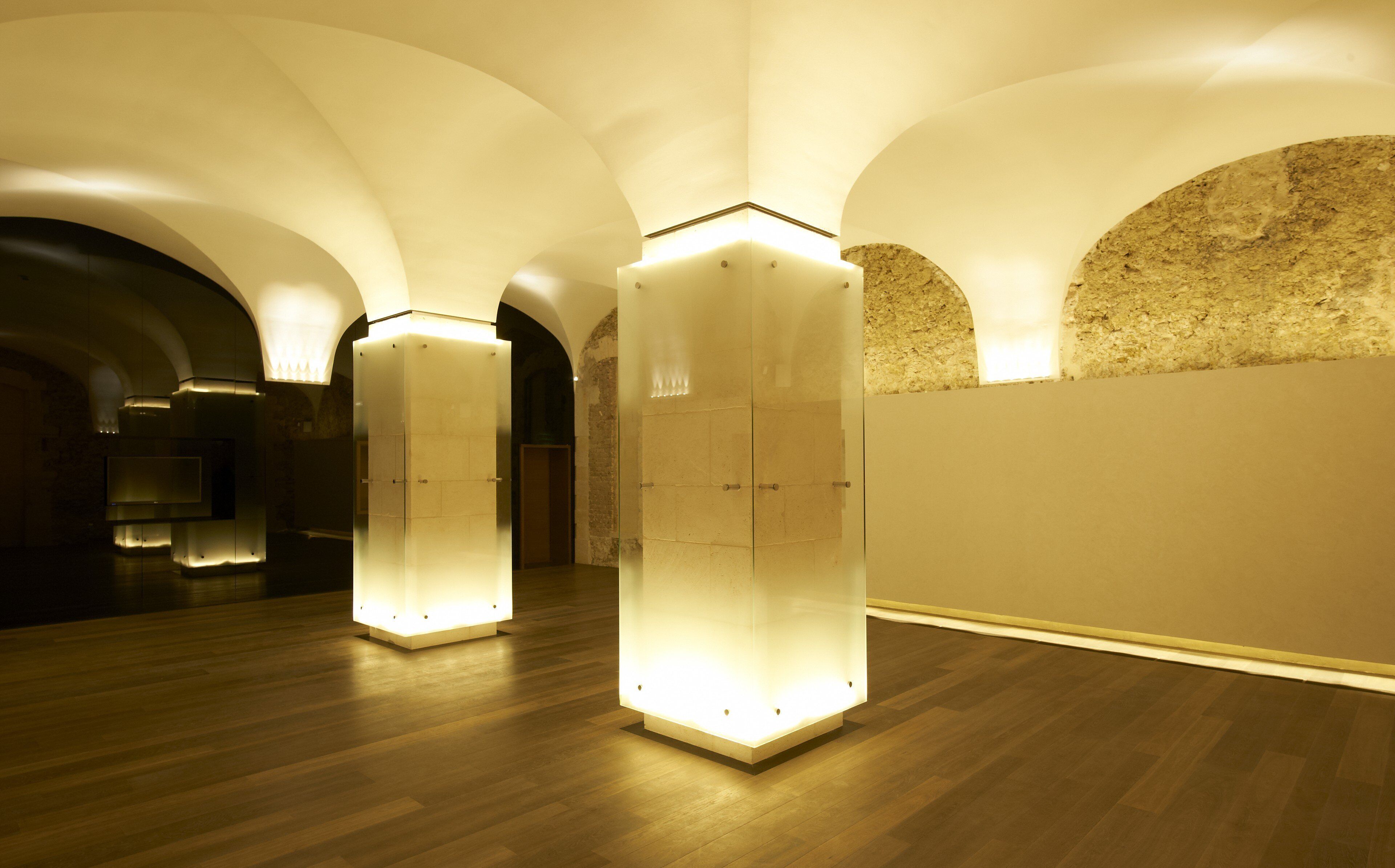 Un couloir aux plafonds voûtés et au plancher en bois, agrémenté de structures carrées illuminées.