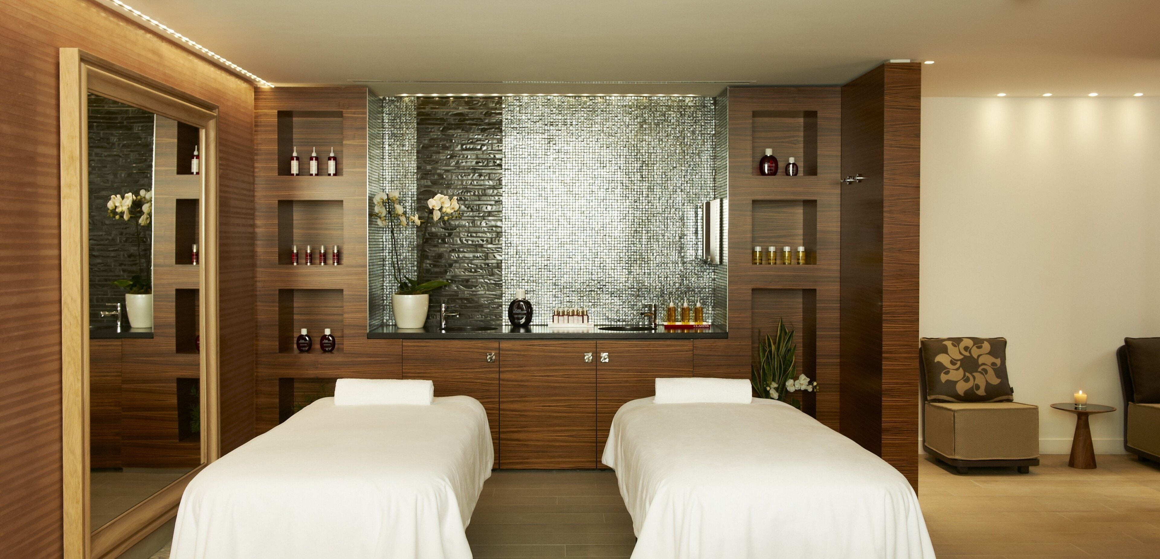 A modern bedroom with two beds, a large mirror, and a wall-mounted vanity with shelves.