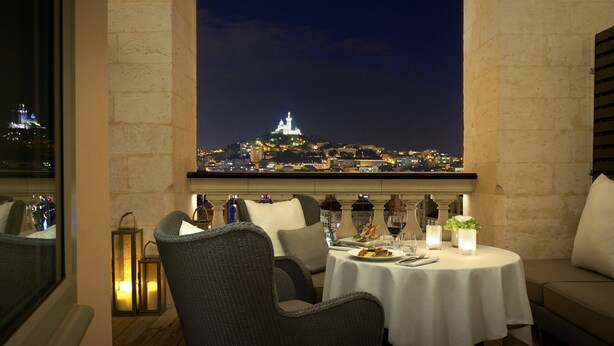 A dining area with wicker chairs, a round table, candles, and a view of a cityscape at night. - InterContinental Marseille - Hotel Dieu by IHG (Marseille)