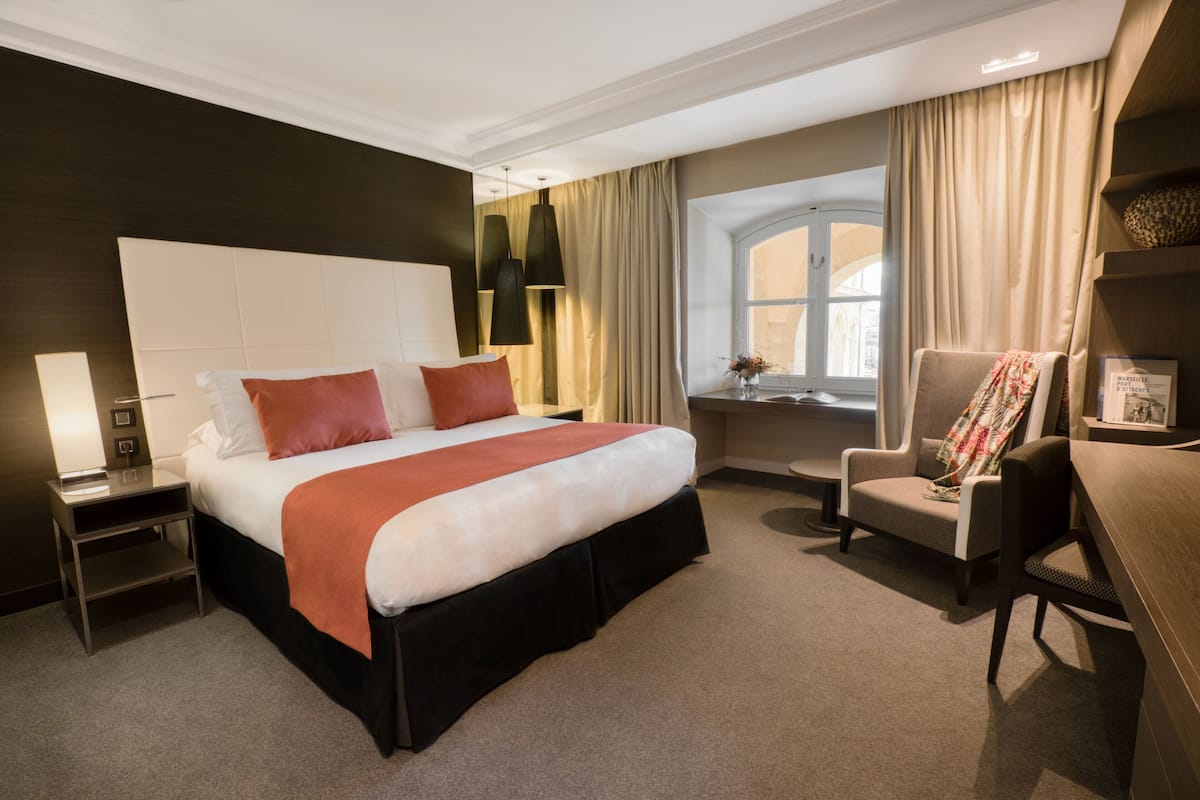 Une chambre d’hôtel moderne avec un grand lit, un bureau, une chaise et une fenêtre avec des rideaux.
