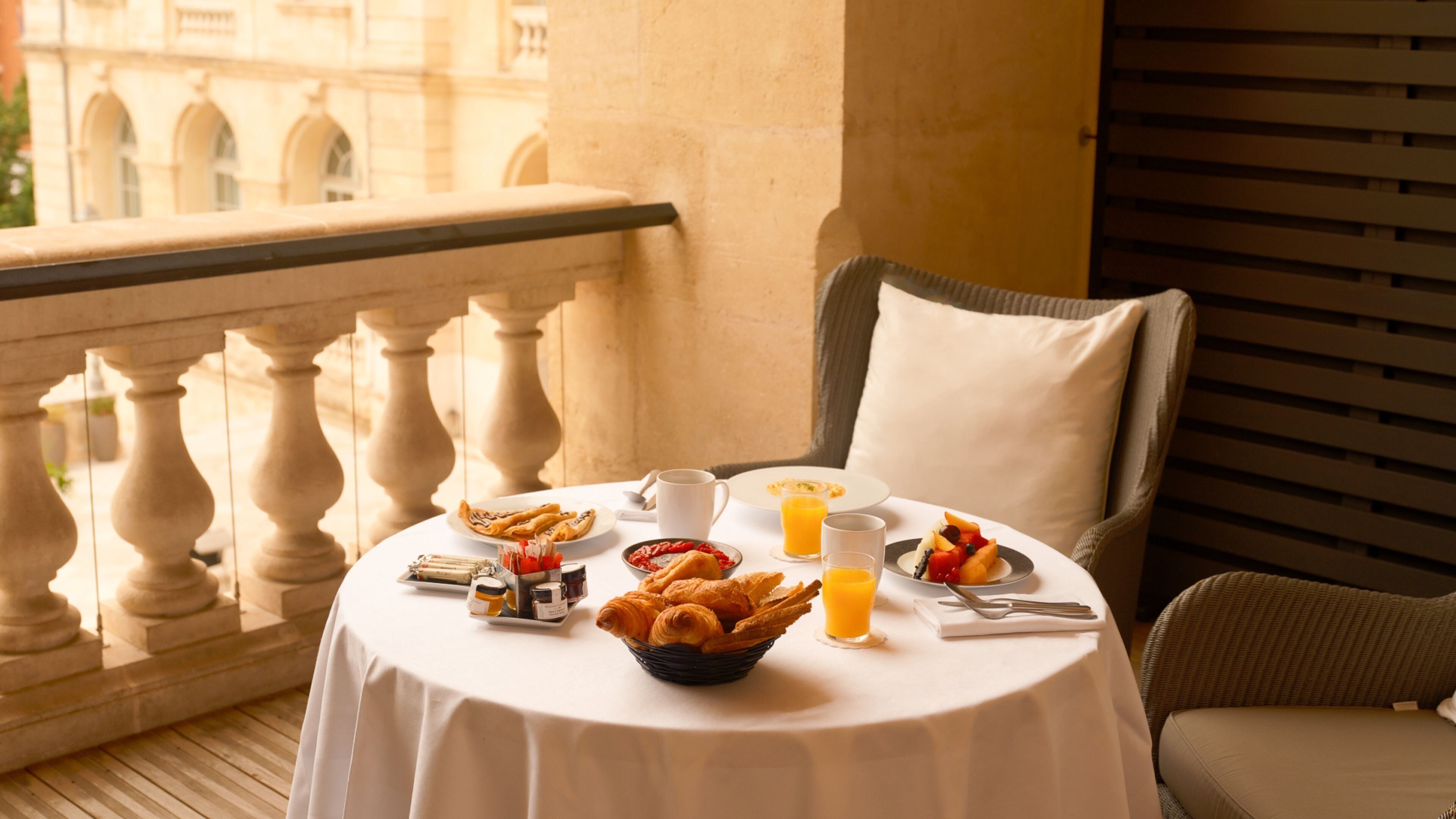 Un balcón con una mesa dispuesta para el desayuno, que incluye cruasanes, fruta y jugo de naranja.