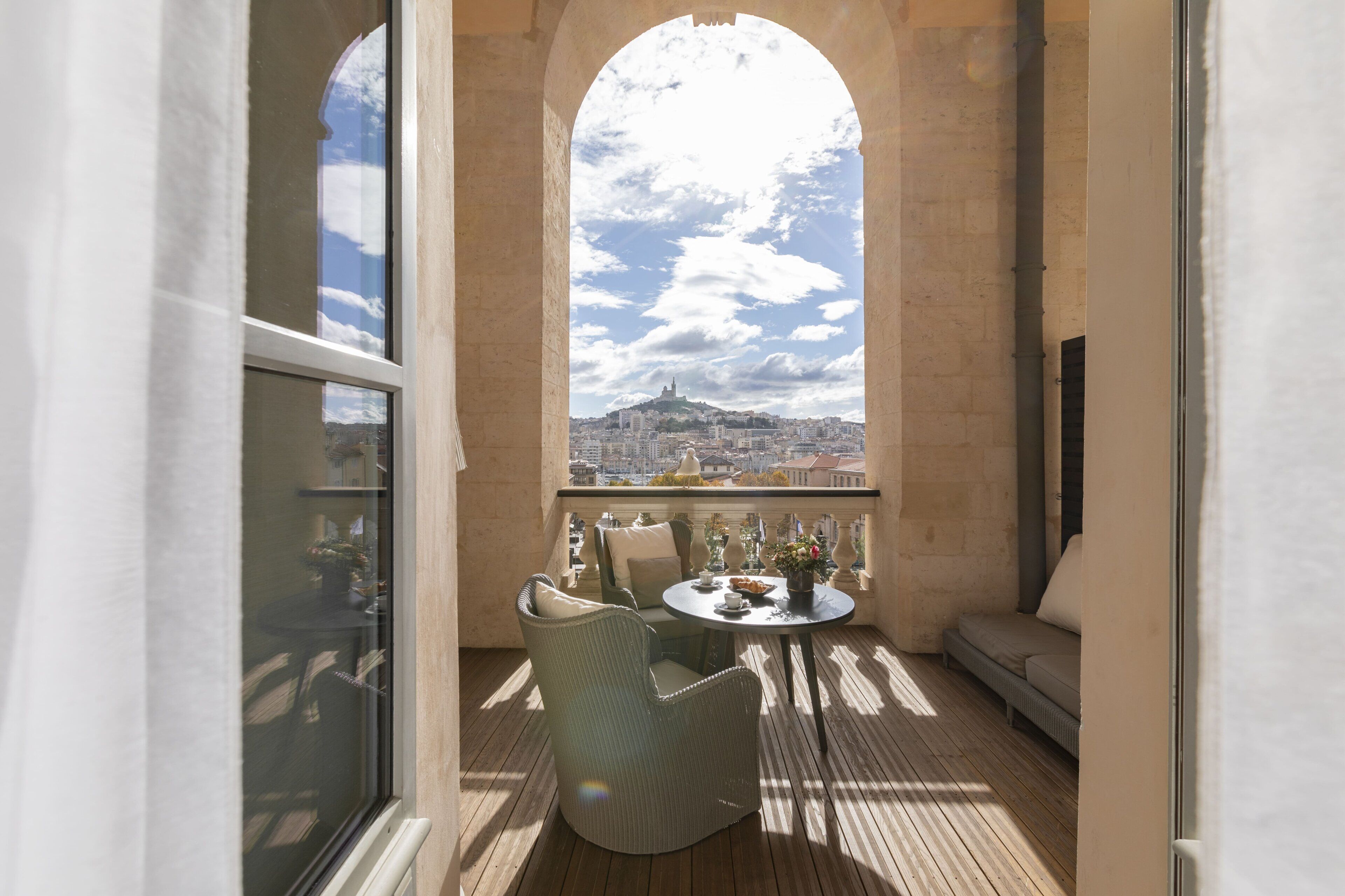 A balcony with wicker furniture, a table with a vase, and a view of a cityscape.