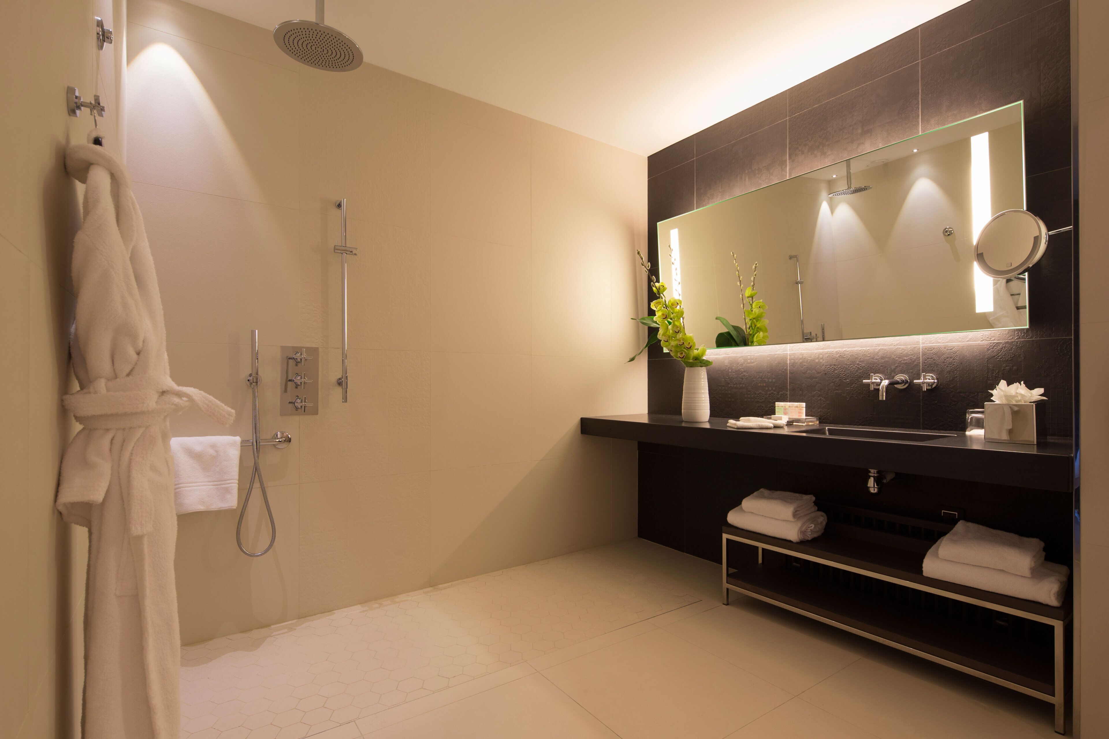 A modern bathroom with a large mirror, a shower, and a vanity with towels.