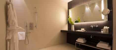 A modern bathroom with a large mirror, a shower, and a vanity with towels.