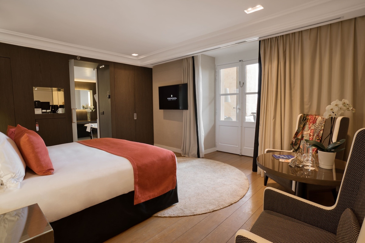 Habitación de hotel con cama, televisión, escritorio con silla y baño visible a través de una puerta abierta.