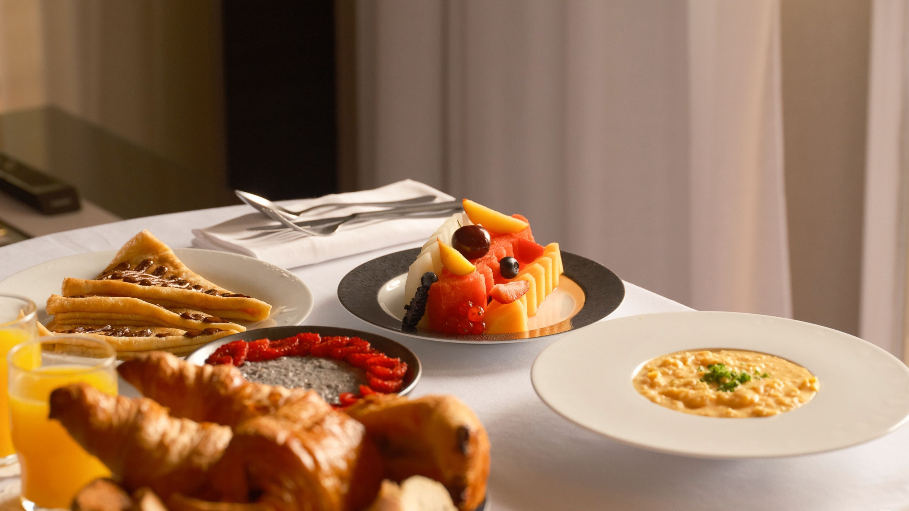 A breakfast table with croissants, fruit, and a bowl of soup.