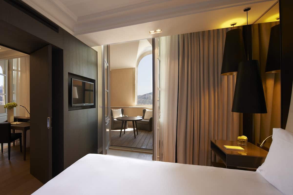 Une chambre d’hôtel avec un grand lit, un bureau avec une chaise, une petite table avec deux chaises et une vue sur la ville par la fenêtre.
