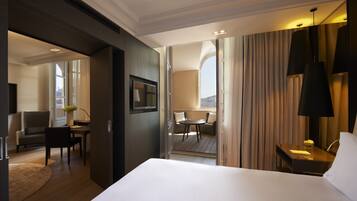 Habitación de hotel con cama, escritorio, silla, una mesita y vistas a la ciudad desde la ventana.