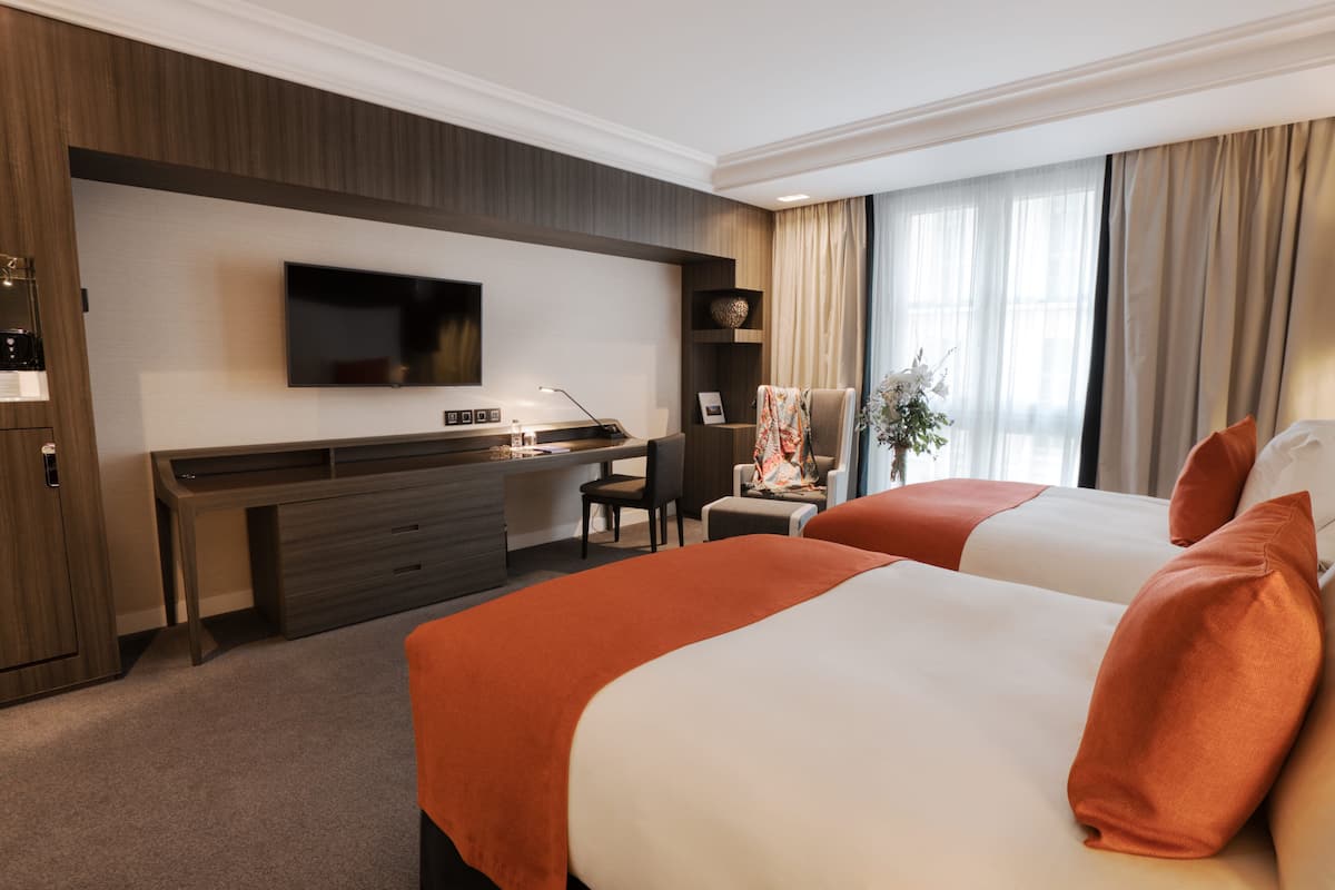 Une chambre d’hôtel avec deux lits, un bureau, une télévision et une fenêtre avec des rideaux.