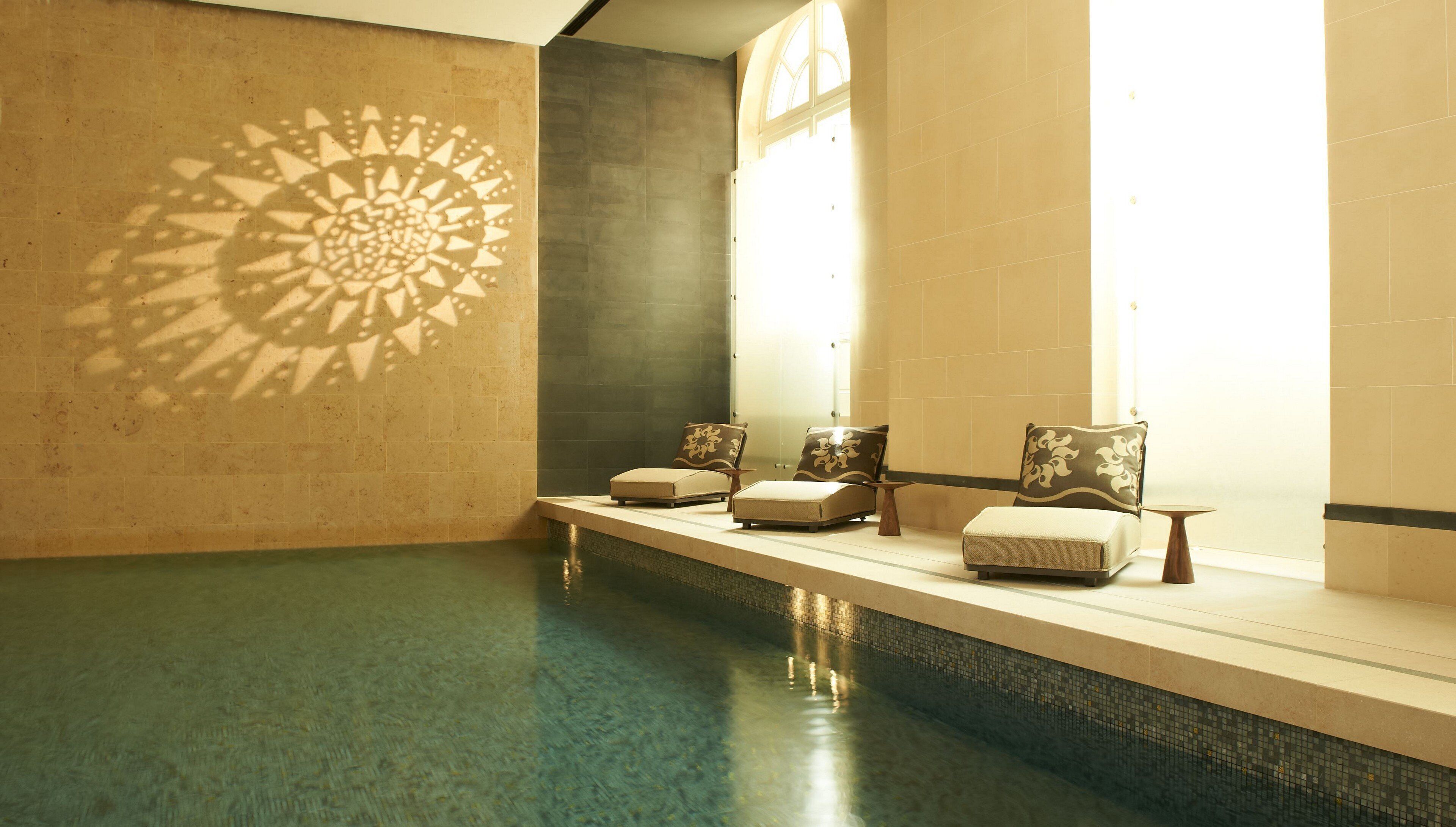 A spa area with a pool, lounge chairs, and a decorative wall pattern.
