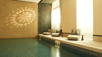 A spa area with a pool, lounge chairs, and a decorative wall pattern.