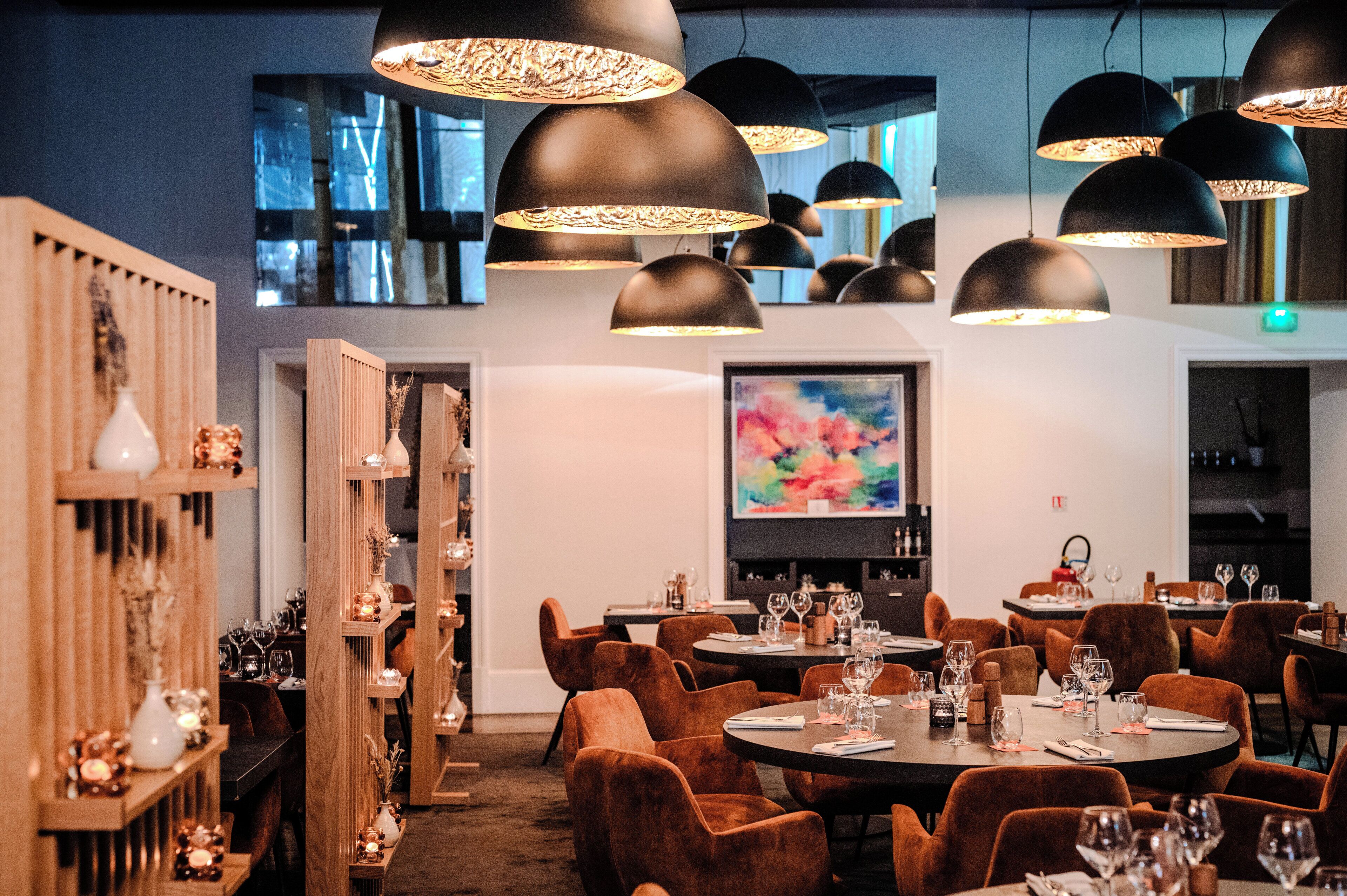 Um restaurante com mesas redondas, cadeiras marrons e luminárias pendentes pretas.