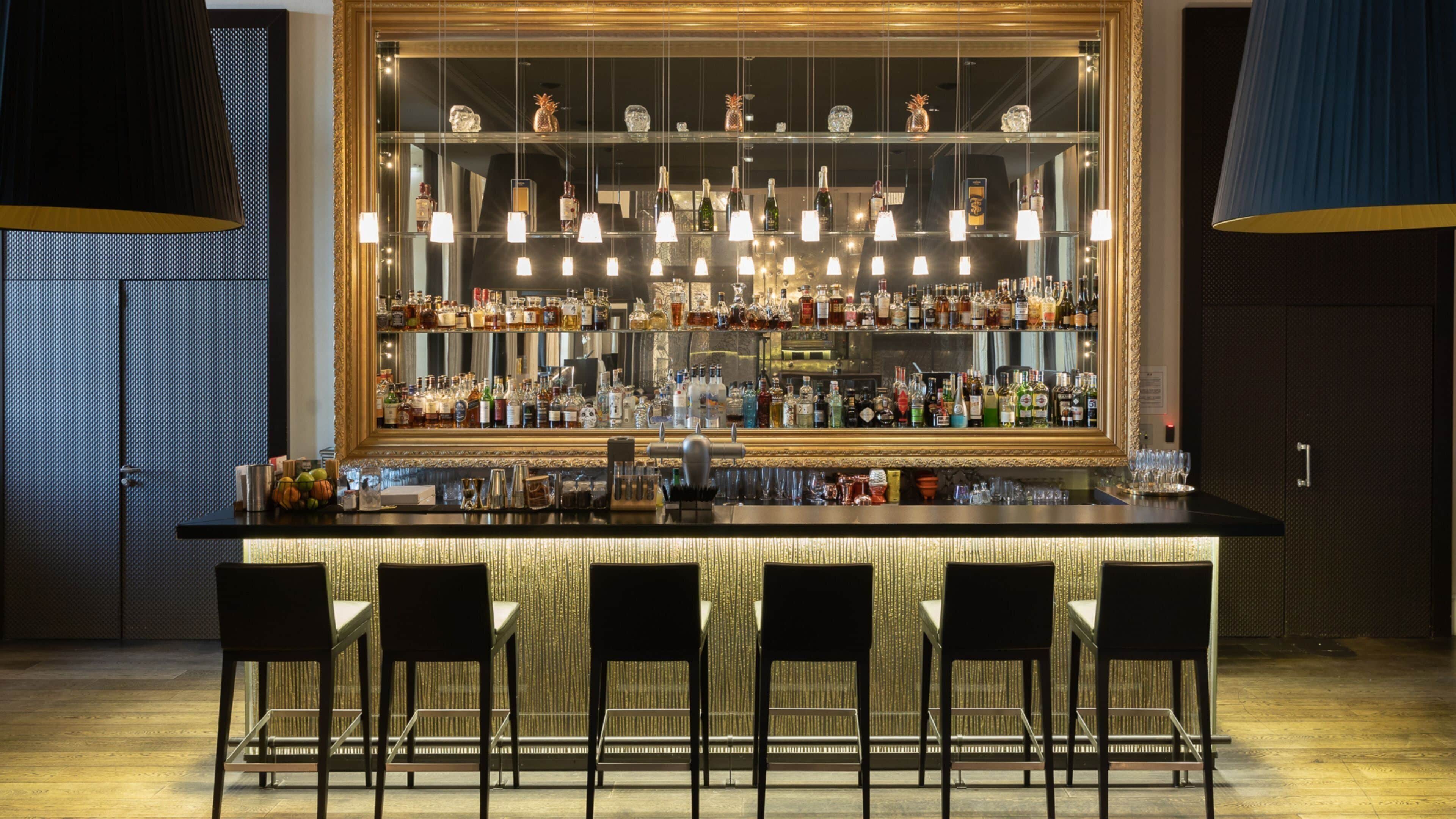 Un bar con pared espejada, múltiples luces colgantes y una variedad de botellas.
