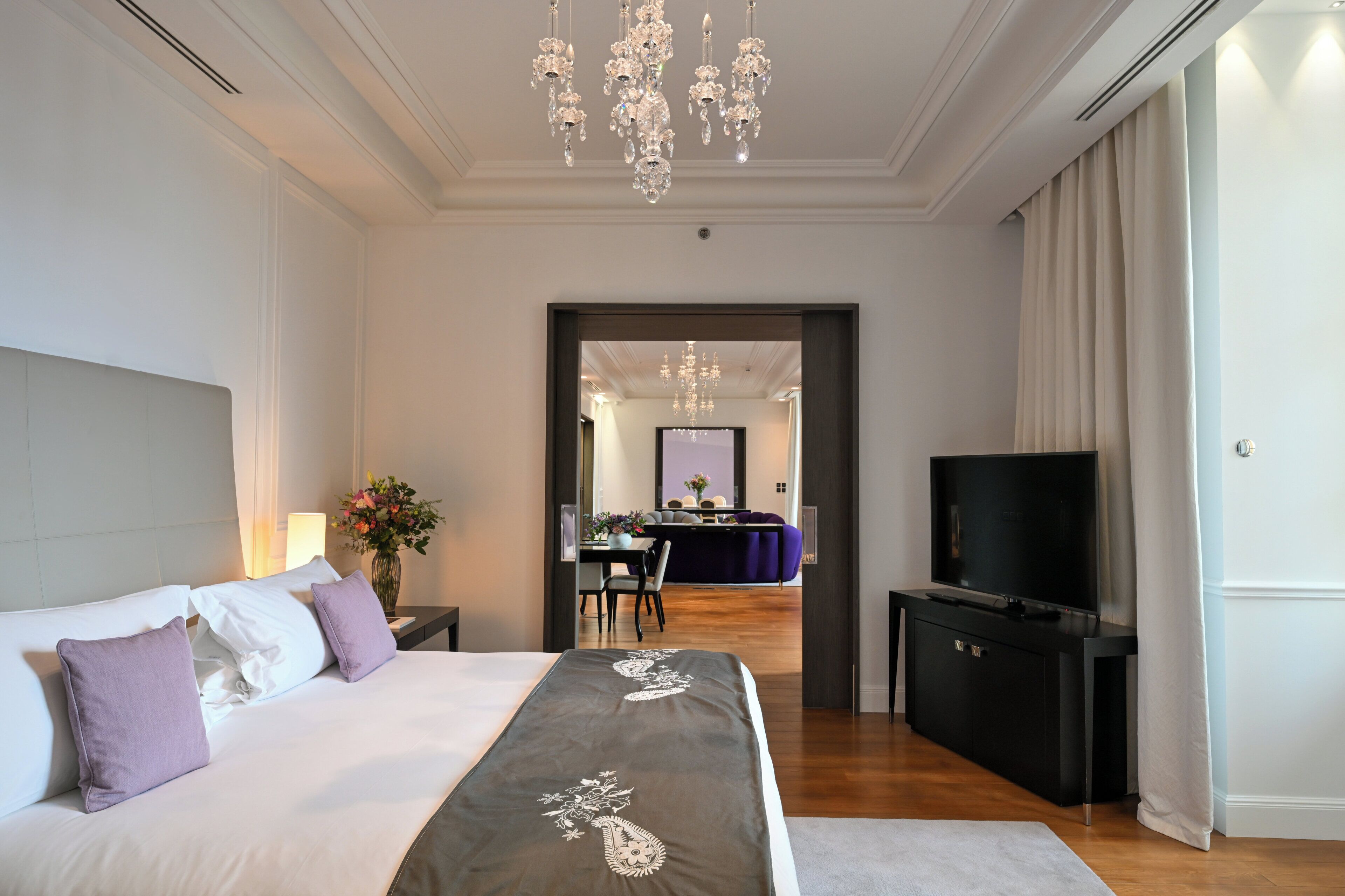 A hotel room with a bed, a TV, a dresser, and a chandelier.