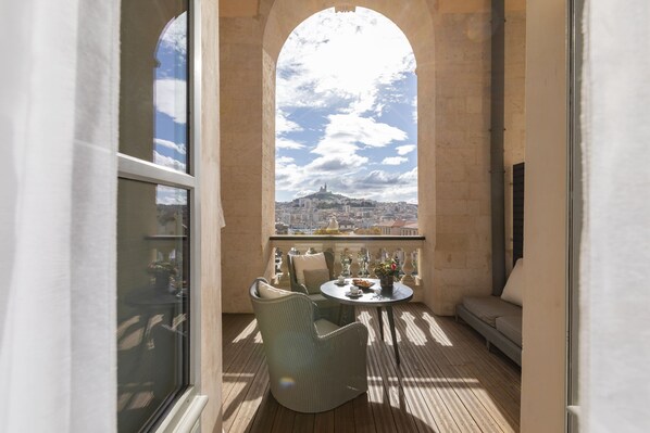 Un balcón con mobiliario de mimbre, una mesa con un florero y vista a un paisaje urbano.
