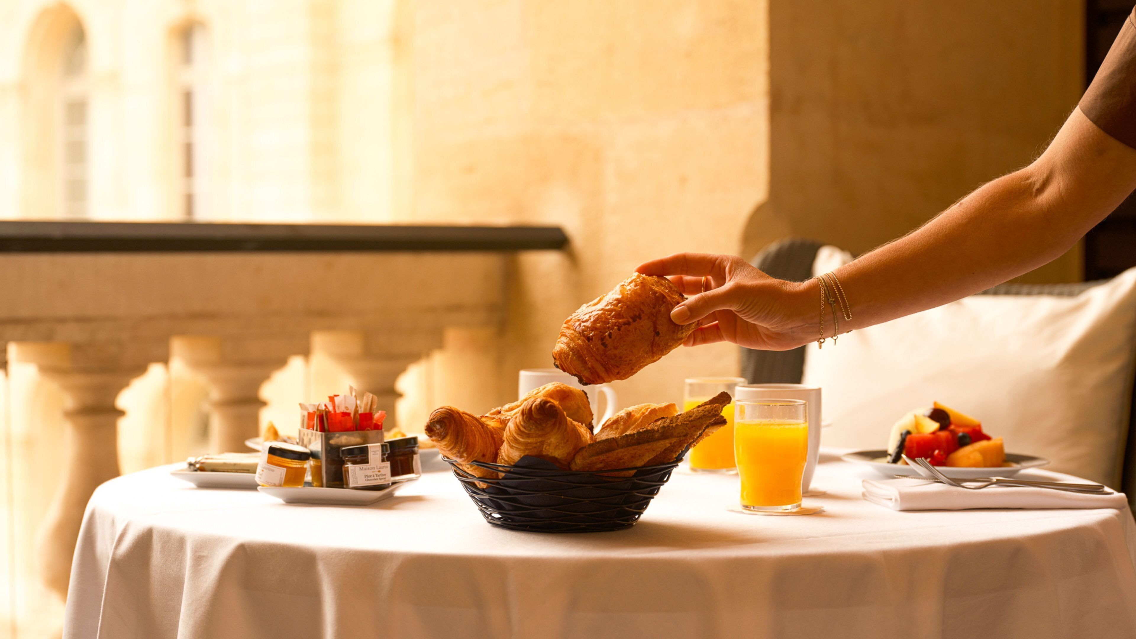 A breakfast setting with croissants, orange juice, and a basket of bread on a table.