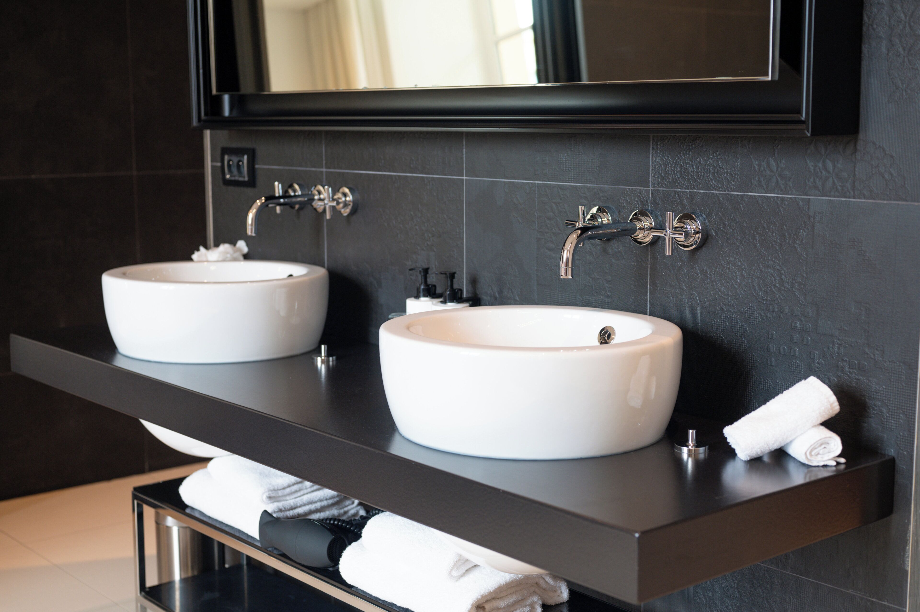 A modern bathroom with two white sinks, a dark countertop, and a mirror above.