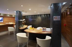 Zona de recepción con un mostrador de madera, sillas blancas, una orquídea en maceta y el logo de spa Clarins.