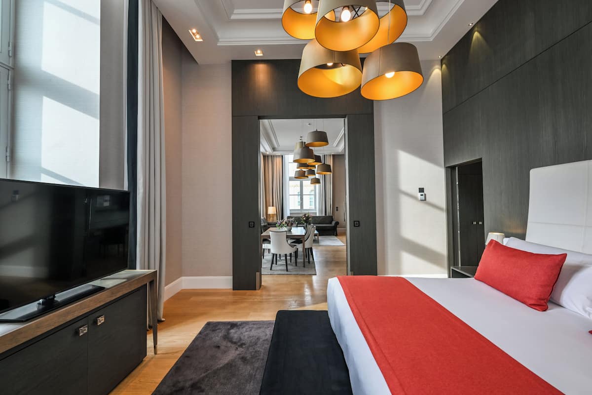 Une chambre d’hôtel moderne avec un grand lit, une télévision et un coin repas à l’arrière-plan.