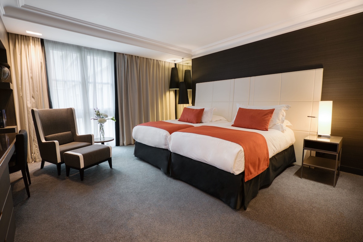 Una habitación de hotel con una cama grande, dos mesitas de noche, una silla y un escritorio.