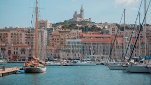 A marina with boats docked, a prominent tower in the background, and buildings with red-tiled roofs. - InterContinental Marseille - Hotel Dieu by IHG (Marseille)