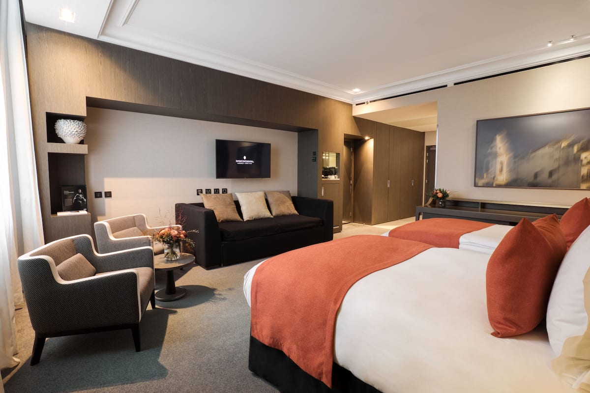 A modern hotel room with a large bed, two armchairs, a sofa, a flat-screen TV, and a painting on the wall.