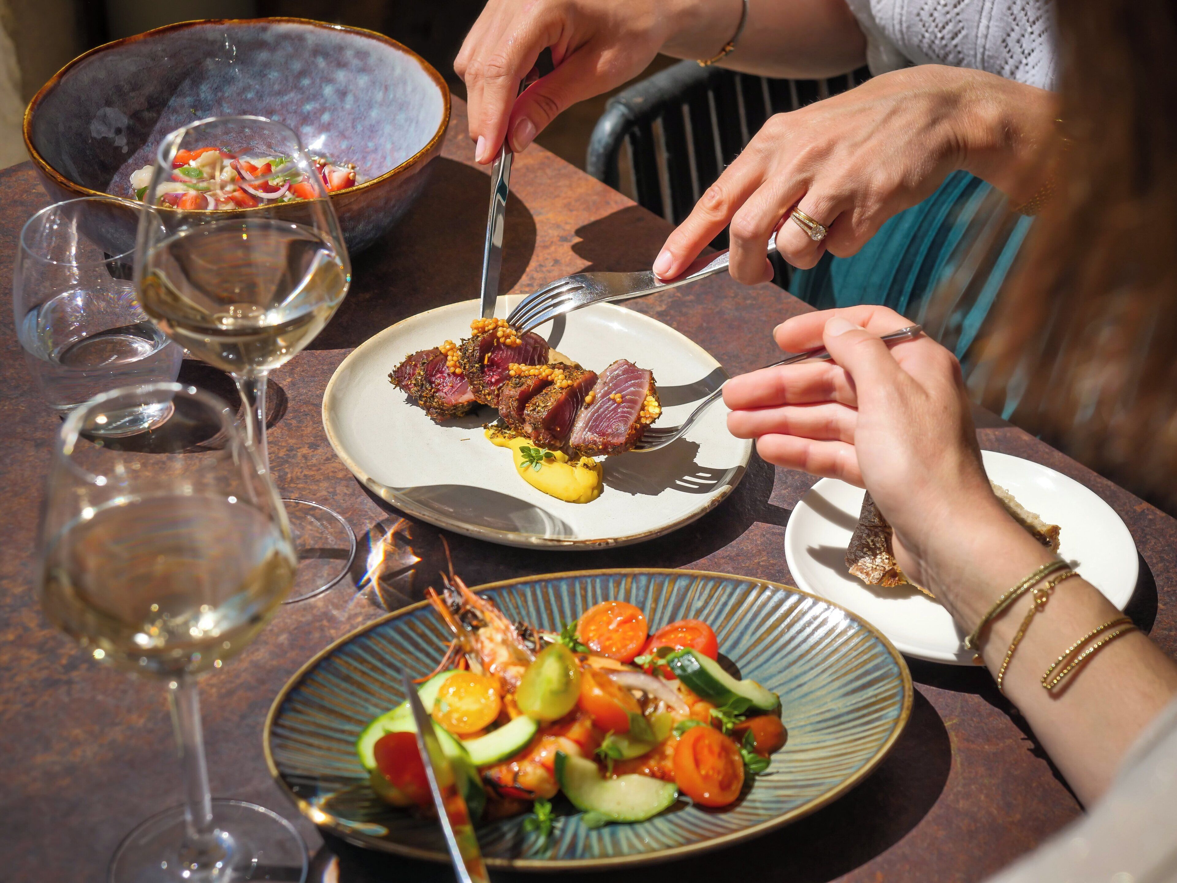 Una mesa con platos de comida, copas de vino y un bol de ensalada.
