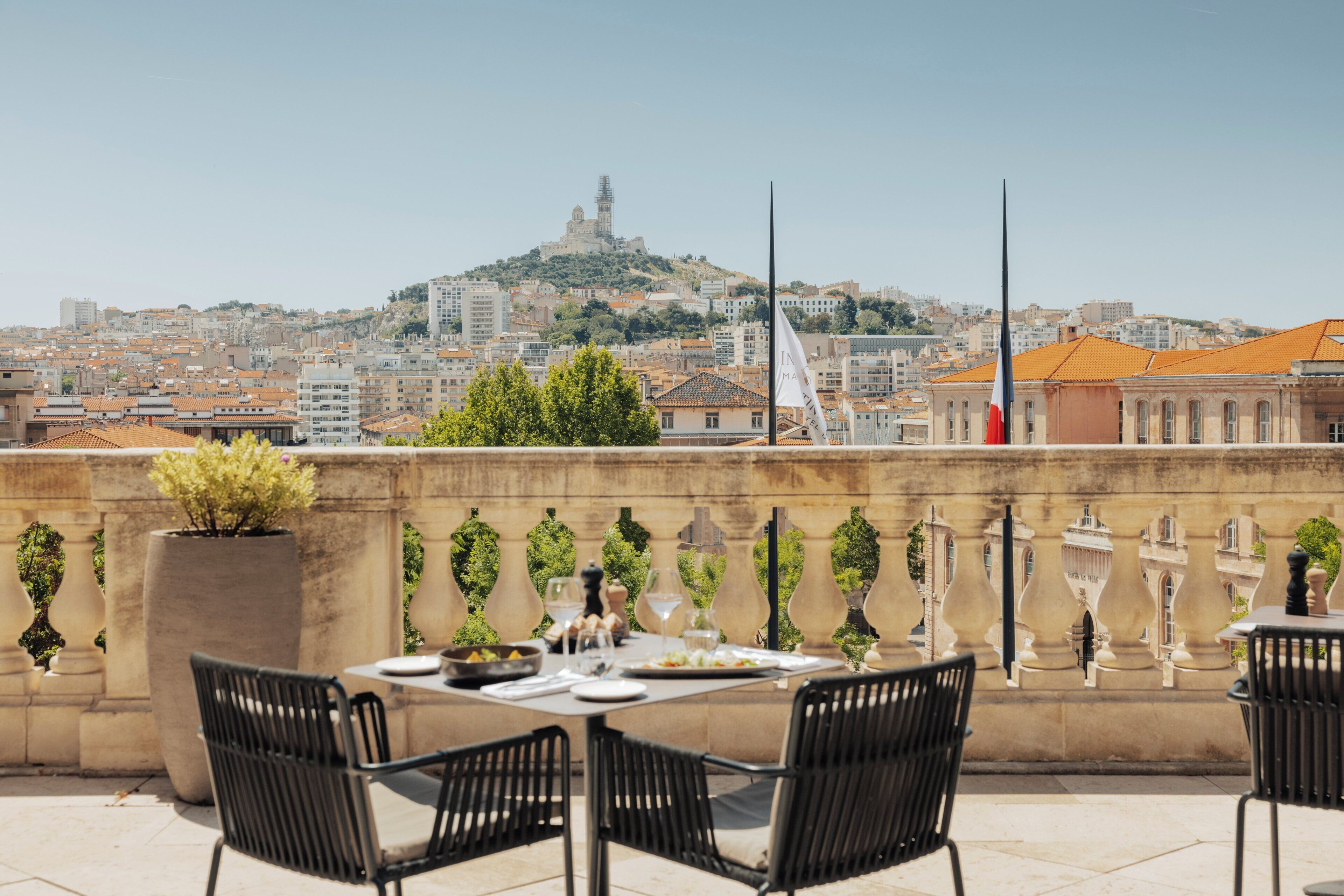 Une terrasse sur le toit, avec une table dressée pour le dîner, des chaises et une vue sur le paysage urbain, avec une colline et des bâtiments.