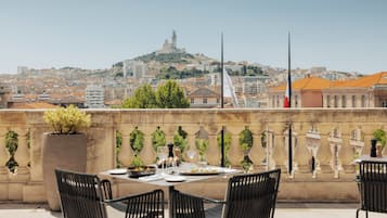 Une terrasse sur le toit, avec une table dressée pour le dîner, des chaises et une vue sur le paysage urbain, avec une colline et des bâtiments.