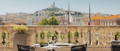 Terraza en la azotea con una mesa dispuesta para comer, sillas y vistas de un paisaje urbano con una colina y edificios.
