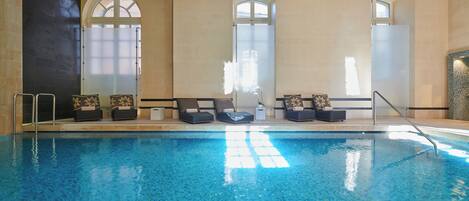 Una piscina interior con sillones de descanso y sombrillas.