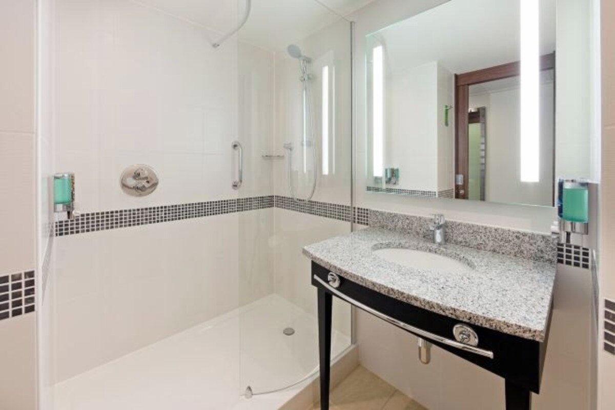 A modern bathroom with a glass-enclosed shower, a white sink with a granite countertop, and a mirror above the sink.