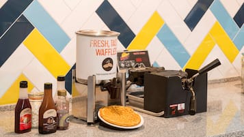 Una máquina para hacer gofres, un gofre y acompañamientos sobre una encimera de cocina.
