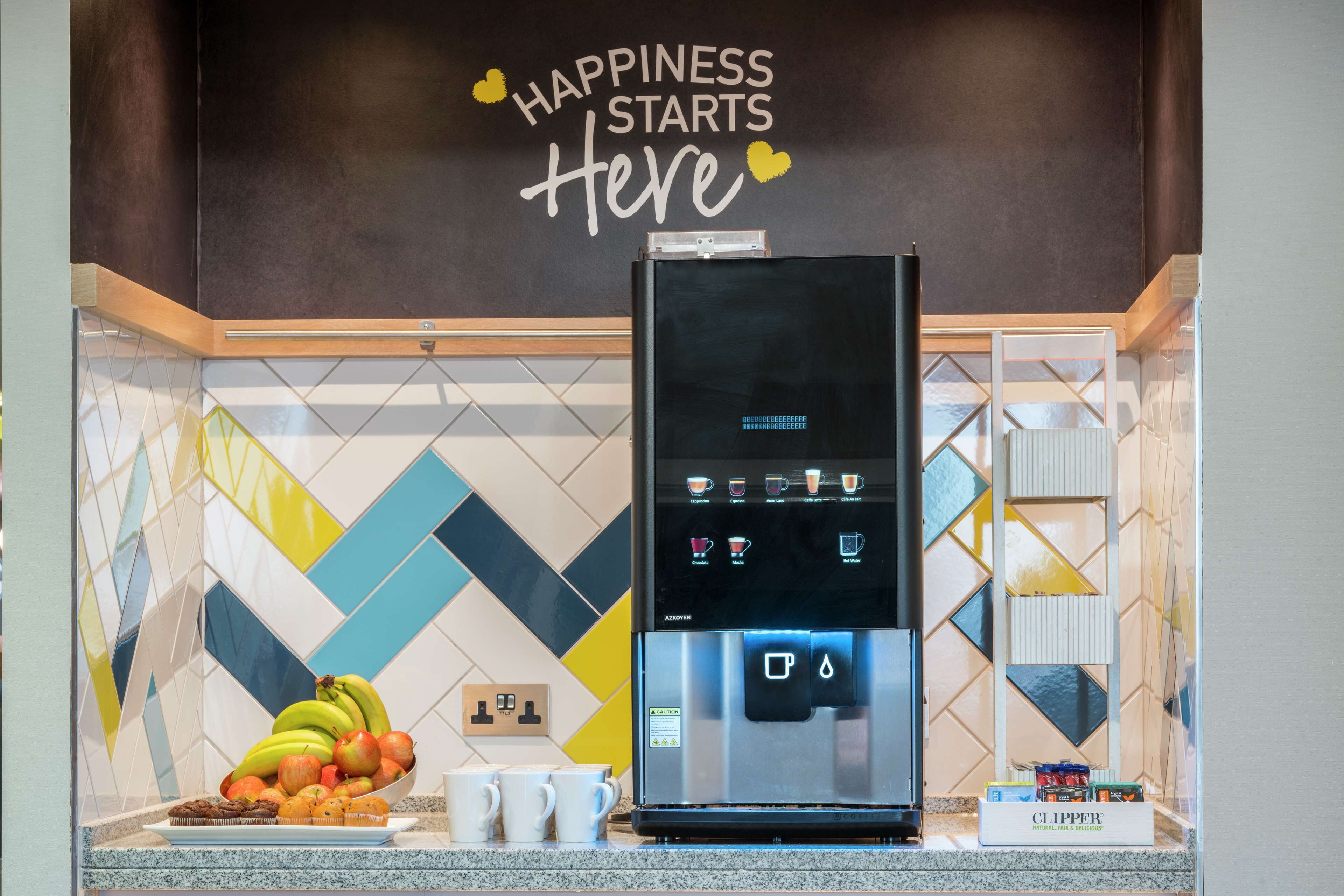 A kitchen with a coffee machine, a bowl of fruit, and a sign that says "Happiness Starts Here".