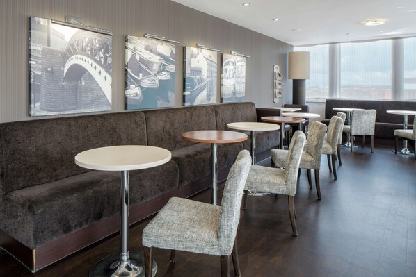 A modern hotel lobby with a grey sofa, round tables, and patterned chairs. - Hampton by Hilton Birmingham Broad Street (Birmingham)