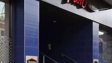 Exterior de un hotel Hampton con un letrero rojo llamativo, paredes azules y una escalera que conduce a la entrada.