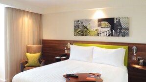 Une chambre d’hôtel avec un grand lit, une tête de lit en bois, une table de chevet, une lampe et un tableau au mur.