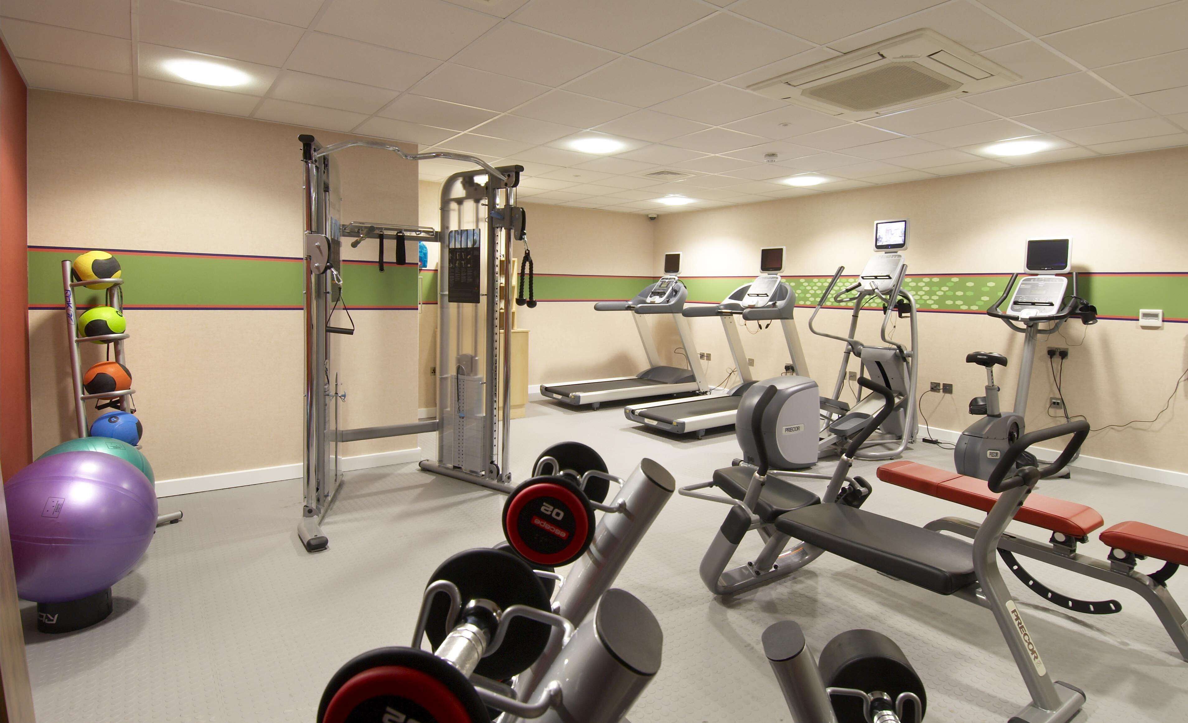 A gym with treadmills, elliptical machines, a bench press, and a rack of medicine balls.