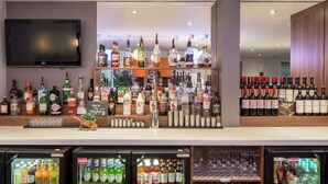 Un espace bar avec un assortiment de bouteilles d’alcool, un téléviseur fixé au mur et un réfrigérateur rempli de boissons.