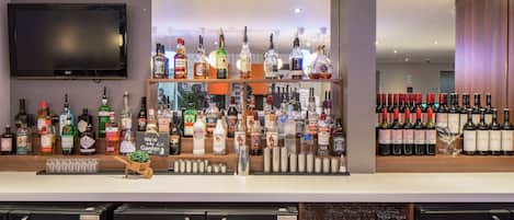 Uma área de bar com diversas garrafas de bebidas alcoólicas, uma televisão presa à parede e um refrigerador cheio de bebidas.