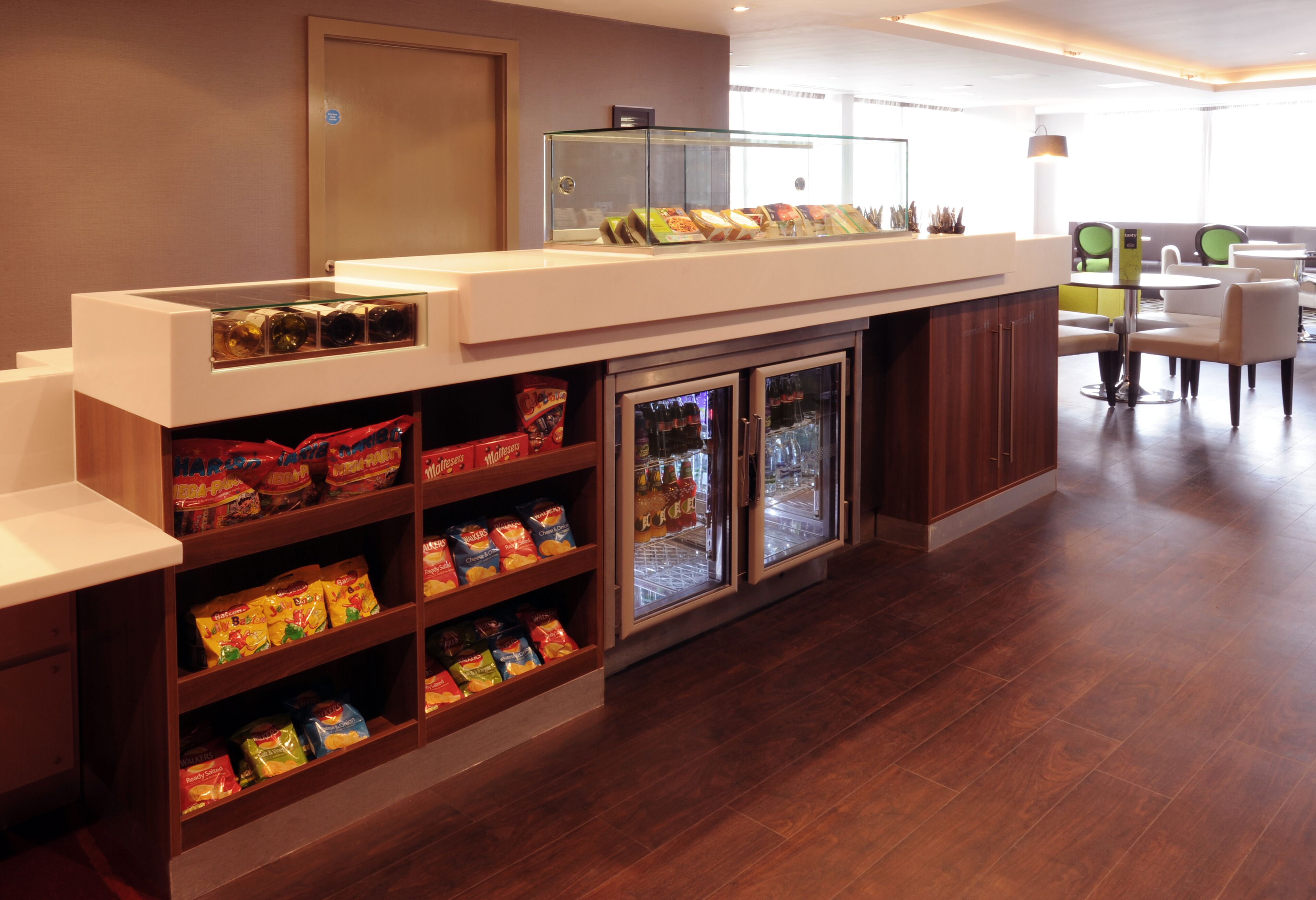 A hotel reception area with a snack bar, refrigerated display cases, and seating area.