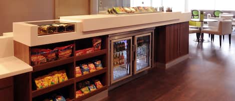 A hotel reception area with a snack bar, refrigerated display cases, and seating area.